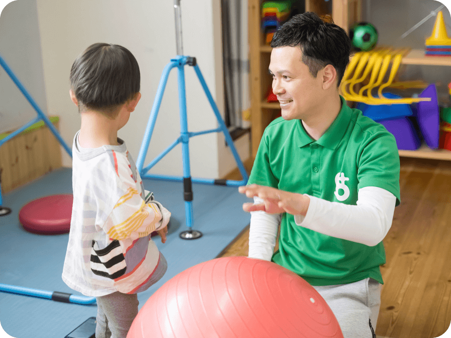 画像：バランスボールや鉄棒のある部屋で話すスタッフと子供